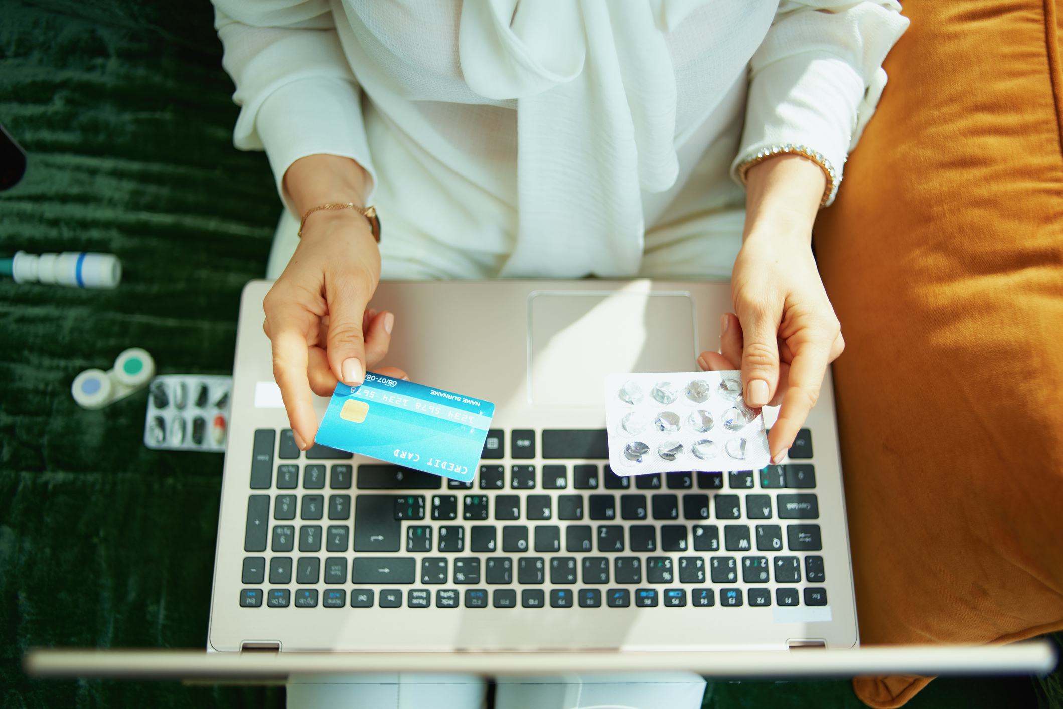 Upper view of woman with credit card and empty blister pack of pills buying pharmacy online using laptop at home in sunny day.