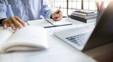Asian businessman sit at desk work on laptop making notes. watch webinar or training course via laptop computer, study and work online from home.