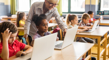 Happy female teacher assisting school kids during an e-learning class at elementary school.